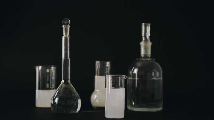 Close-up of various laboratory glassware filled with liquids on a dark background.